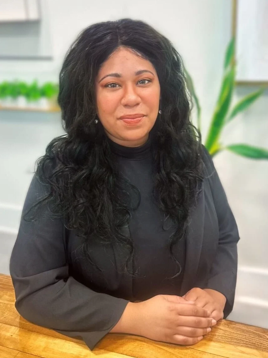 A woman with long black hair sitting in front of plants.