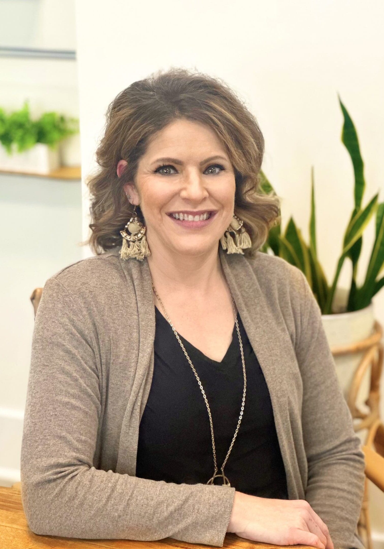 A woman in black shirt and brown jacket near plant.