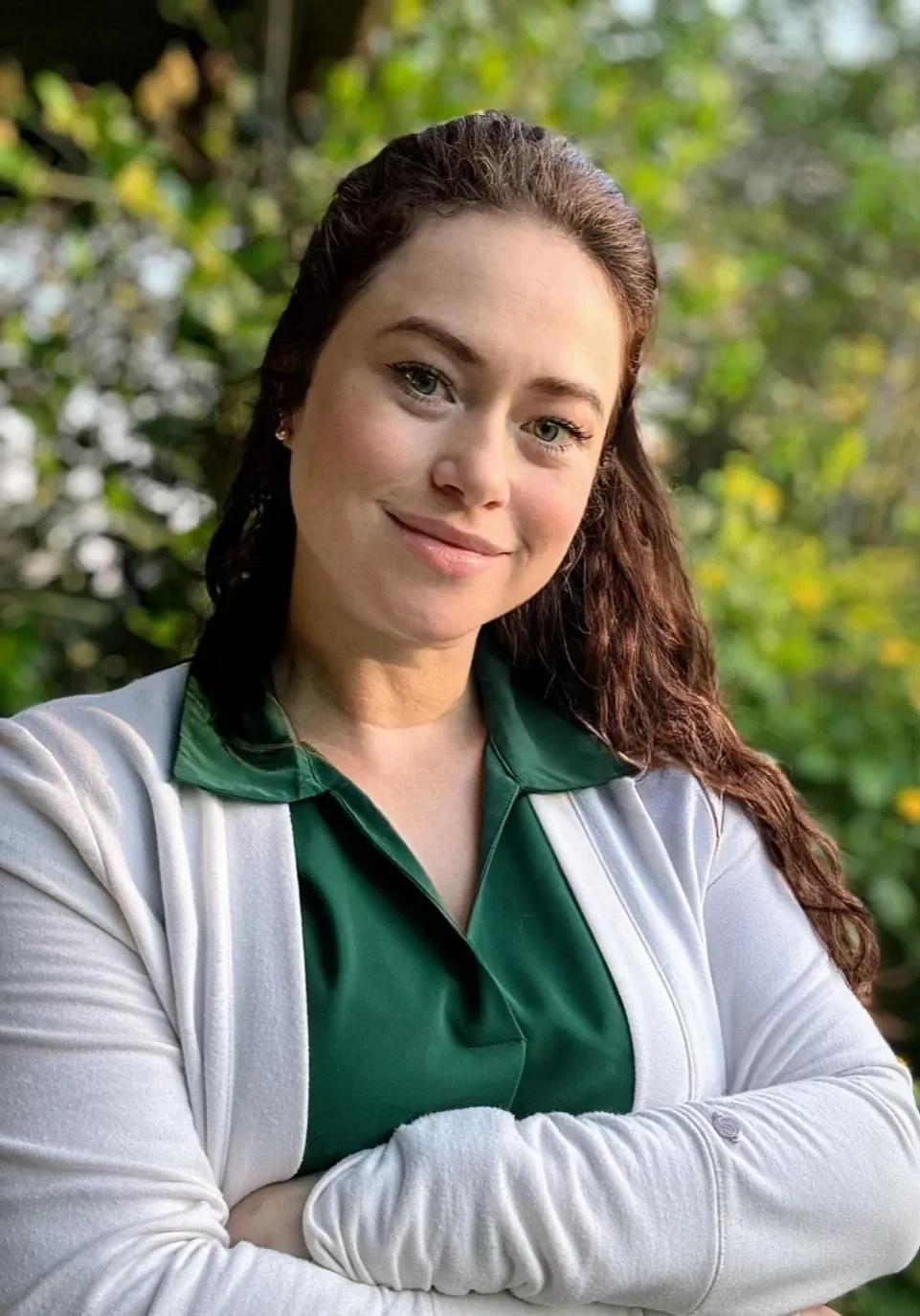 A woman with long hair and green shirt standing in front of trees.